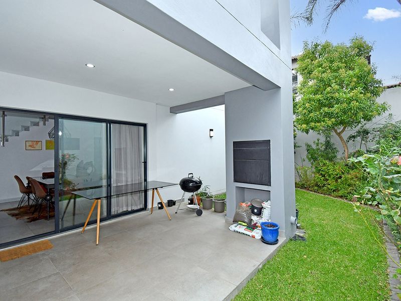 Covered patio area featuring tiled flooring, recessed lighting, and a built-in braai, providing seamless access to the garden through large sliding glass doors.