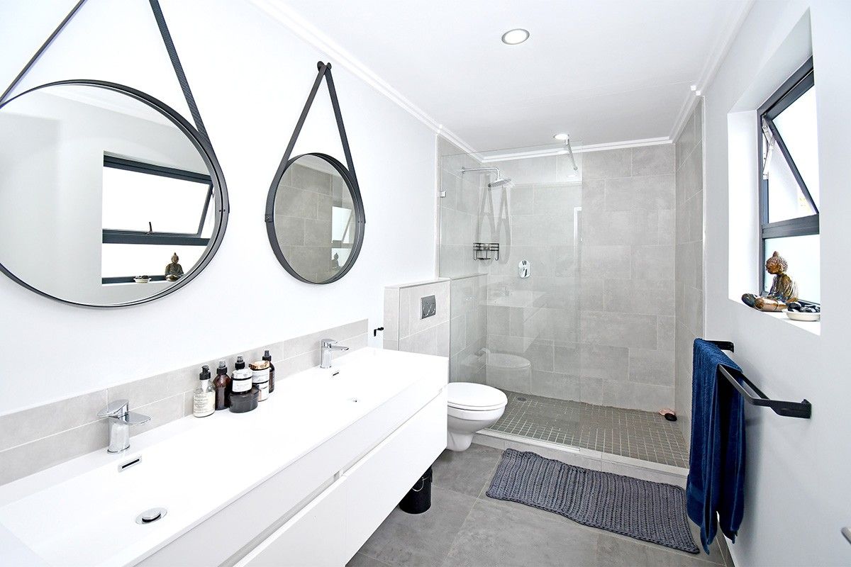 Modern bathroom featuring a sleek double vanity, wall-mounted toilet, and a spacious walk-in shower with glass enclosure and neutral tiling.