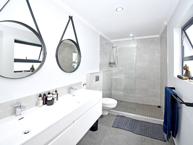 Modern bathroom featuring a sleek double vanity, wall-mounted toilet, and a spacious walk-in shower with glass enclosure and neutral tiling.