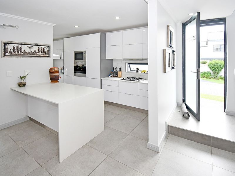Modern kitchen featuring sleek white cabinetry, a central island, built-in appliances, and tiled flooring, with direct access to the exterior.