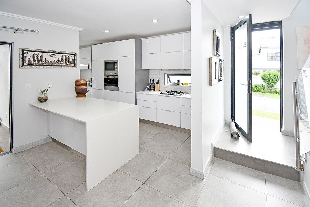 Modern kitchen featuring sleek white cabinetry, a central island, built-in appliances, and tiled flooring, with direct access to the exterior.