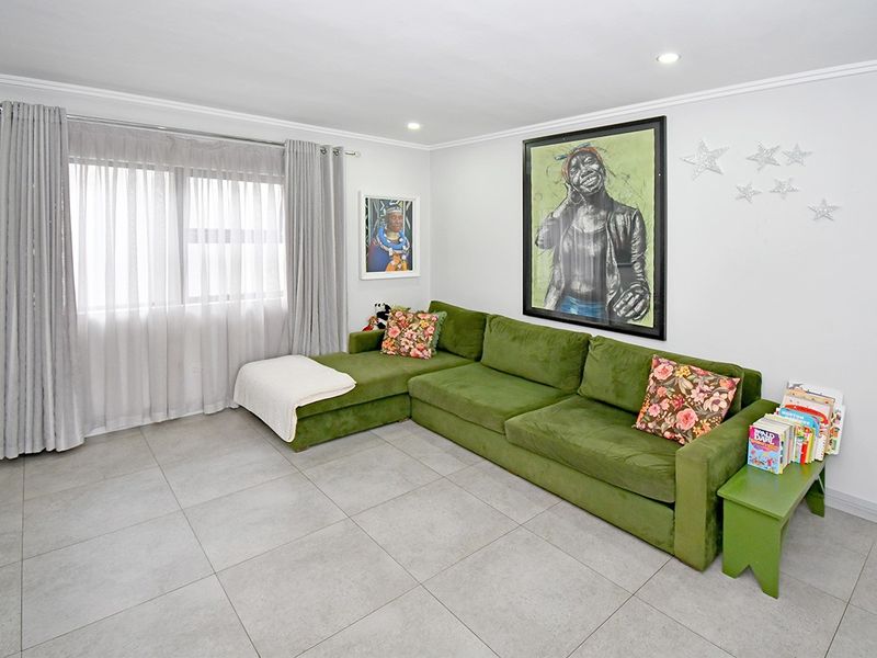 A bright and well-maintained living room featuring neutral tiled flooring, recessed downlighting, and coving detail.
