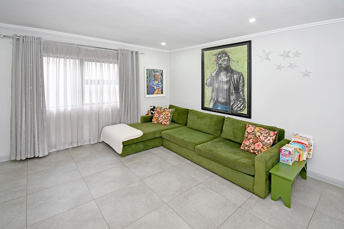 A bright and well-maintained living room featuring neutral tiled flooring, recessed downlighting, and coving detail.
