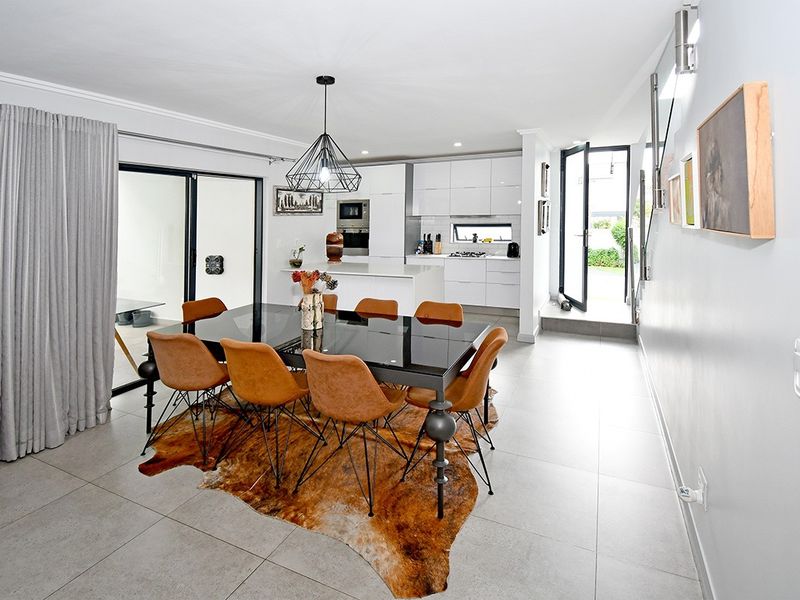 Modern open-plan living and dining area featuring a sleek kitchen with built-in appliances, tiled floors, and seamless access to outdoor spaces.