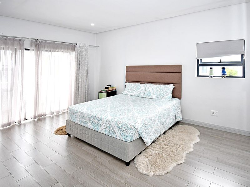A bright and spacious bedroom featuring modern tiled flooring, recessed lighting, and large sliding glass doors that provide ample natural light.