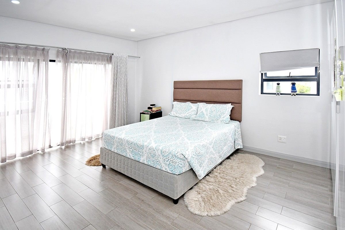 A bright and spacious bedroom featuring modern tiled flooring, recessed lighting, and large sliding glass doors that provide ample natural light.