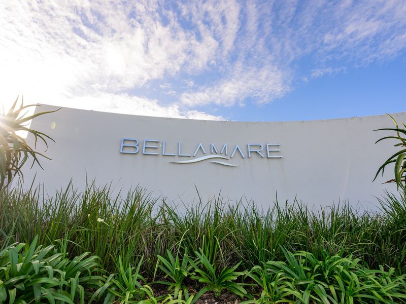 The entrance signage for the Bellamare apartment complex, featuring modern lettering set against a curved wall with surrounding landscaped greenery.