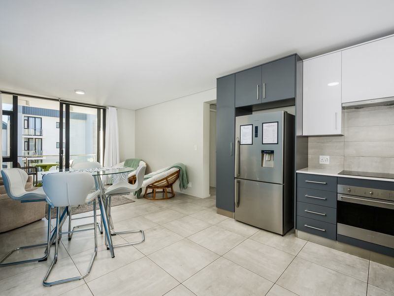 Modern open-plan living area featuring a contemporary kitchen with sleek cabinetry, integrated appliances, and direct access to a private balcony through sliding glass doors.