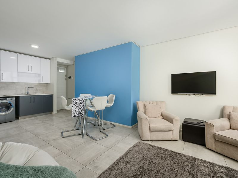 Modern open-plan living area featuring a compact kitchen with built-in cabinetry, tiled flooring, and a bright blue accent wall.