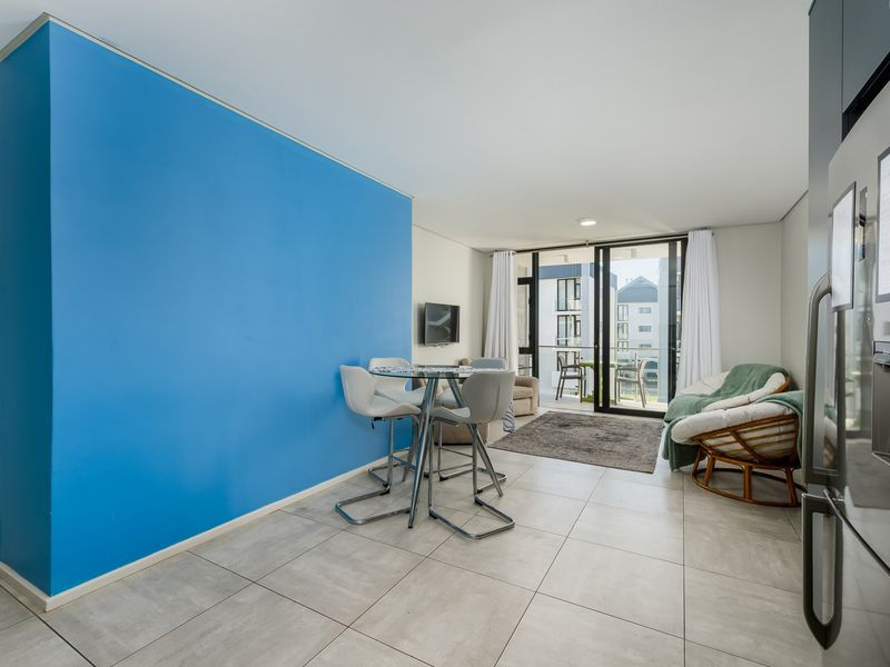Open-plan living area featuring large format floor tiles, a vibrant blue accent wall, and direct access to a private balcony through sliding glass doors.