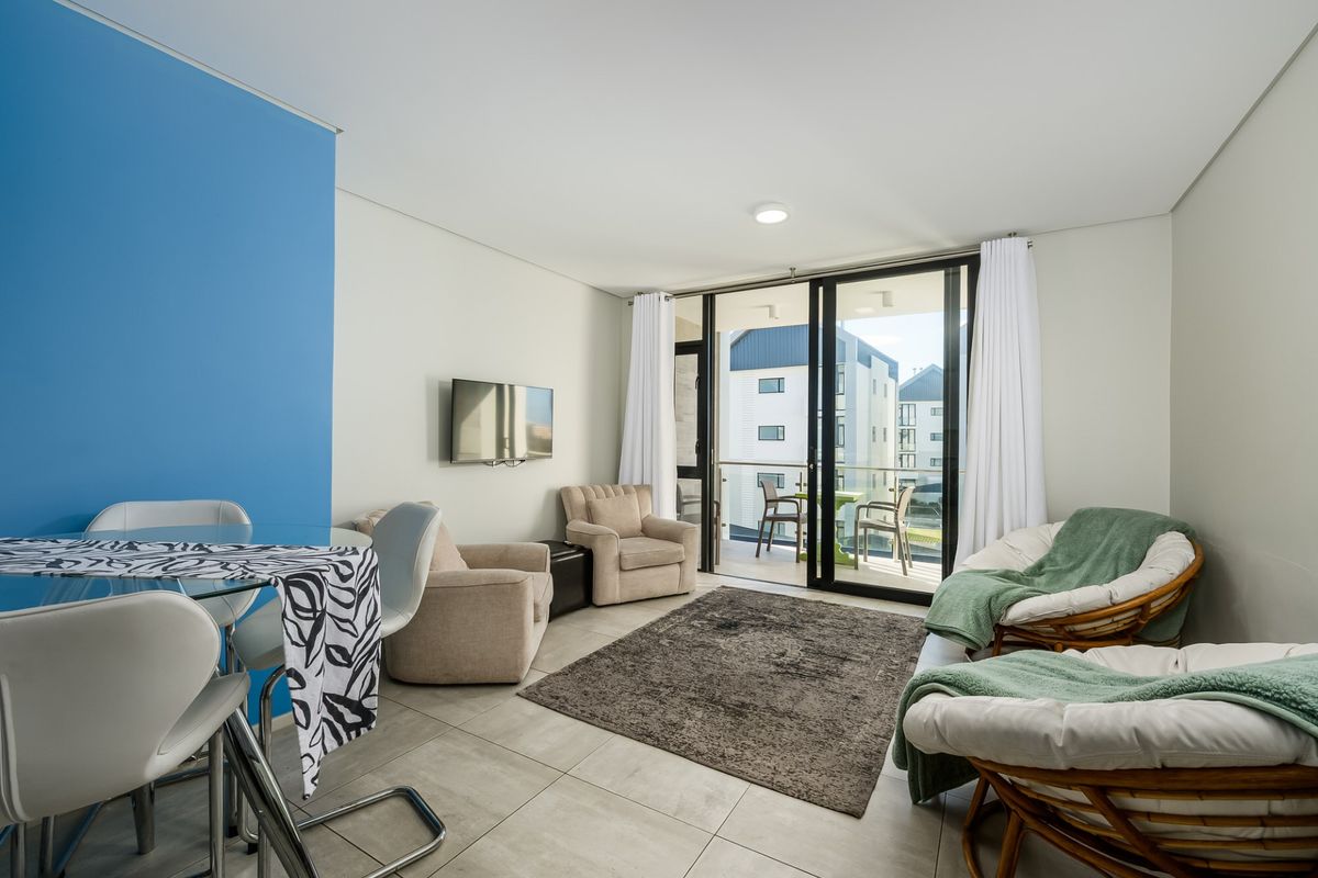 Bright open-plan living area featuring large sliding glass doors leading to a private balcony, neutral tiled flooring, and a modern blue accent wall.