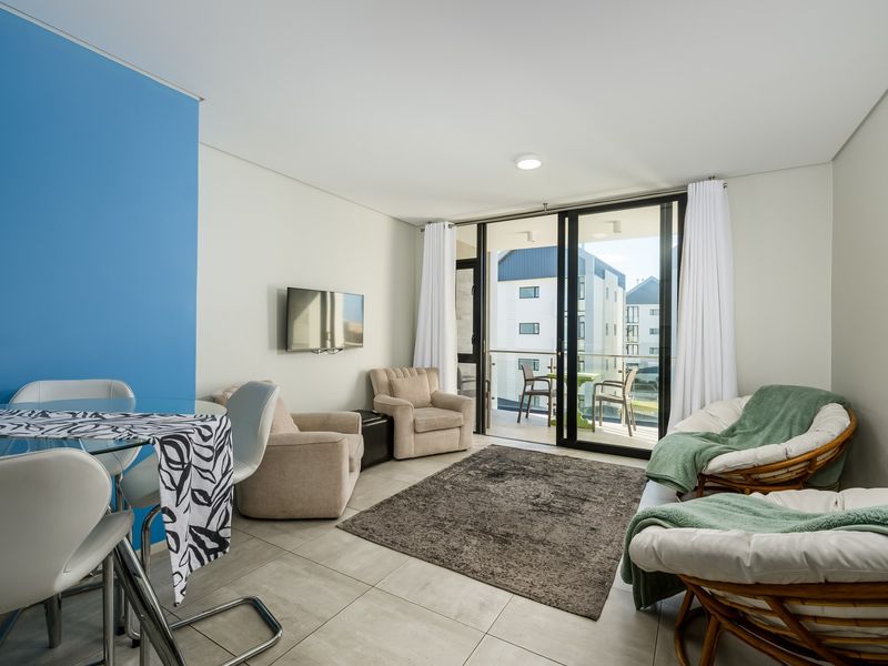 Bright open-plan living area featuring large sliding glass doors leading to a private balcony, neutral tiled flooring, and a modern blue accent wall.