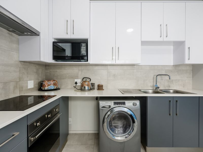 Modern kitchen featuring sleek two-tone cabinetry, stone countertops, integrated appliances, and a tiled splashback.