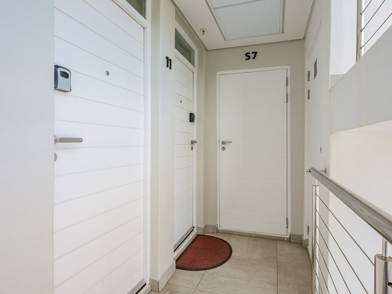 A clean and well-maintained apartment hallway featuring tiled flooring, secure entry doors, and a modern stainless steel balustrade.
