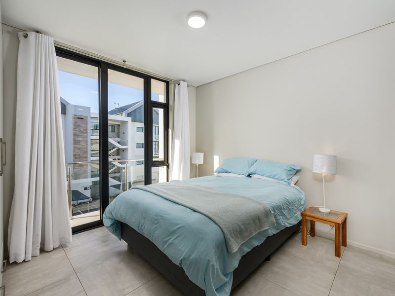 Modern bedroom featuring large floor-to-ceiling sliding glass doors that open onto a private balcony, providing ample natural light and contemporary tiled flooring.