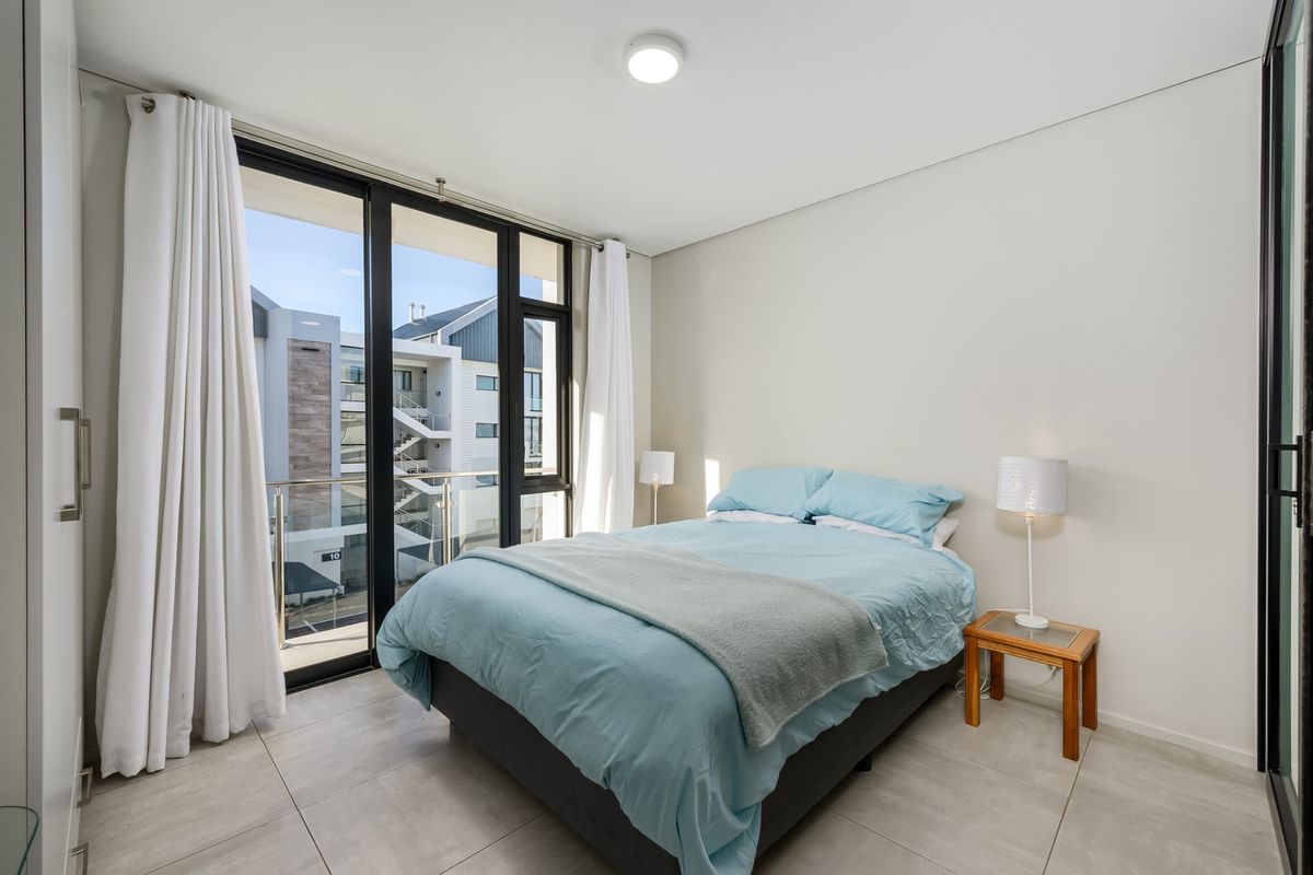 Modern bedroom featuring large floor-to-ceiling sliding glass doors that open onto a private balcony, providing ample natural light and contemporary tiled flooring.