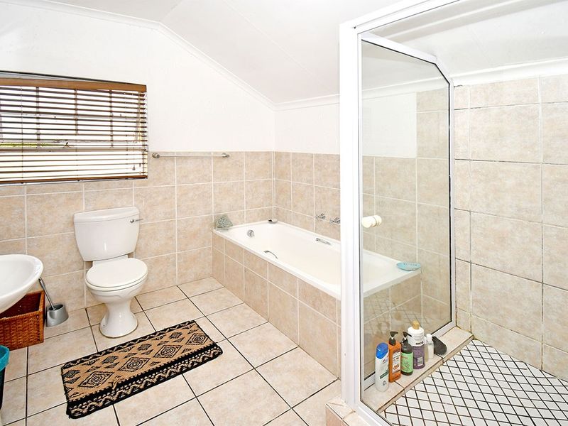 A functional bathroom featuring a pedestal basin, toilet, built-in bathtub, and a separate glass-enclosed shower with neutral wall and floor tiling.