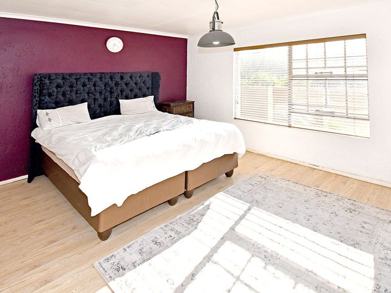 A bedroom featuring laminate flooring, a feature wall, and venetian blinds, providing a functional space with potential for modern updates.