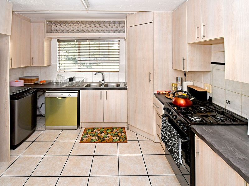 Functional kitchen featuring light wood-look cabinetry, tiled flooring, a gas stove, and a double bowl stainless steel sink with a window view.
