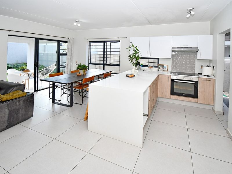 Modern open-plan living and kitchen area featuring a central island, built-in appliances, tiled flooring, and direct access to an outdoor patio space.