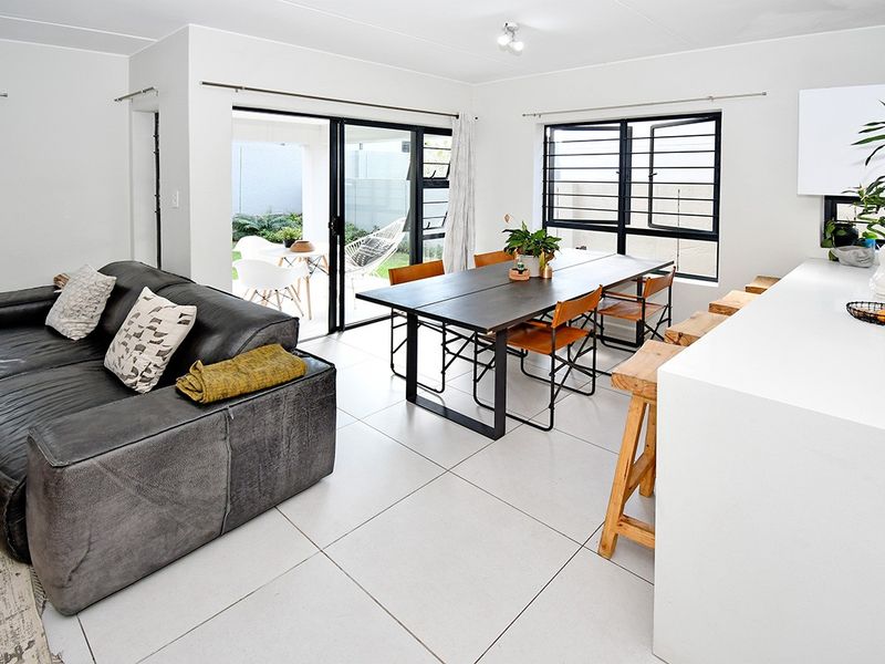 Modern open-plan living and dining area featuring large format floor tiles, a kitchen island, and seamless access to the outdoor patio through sliding doors.