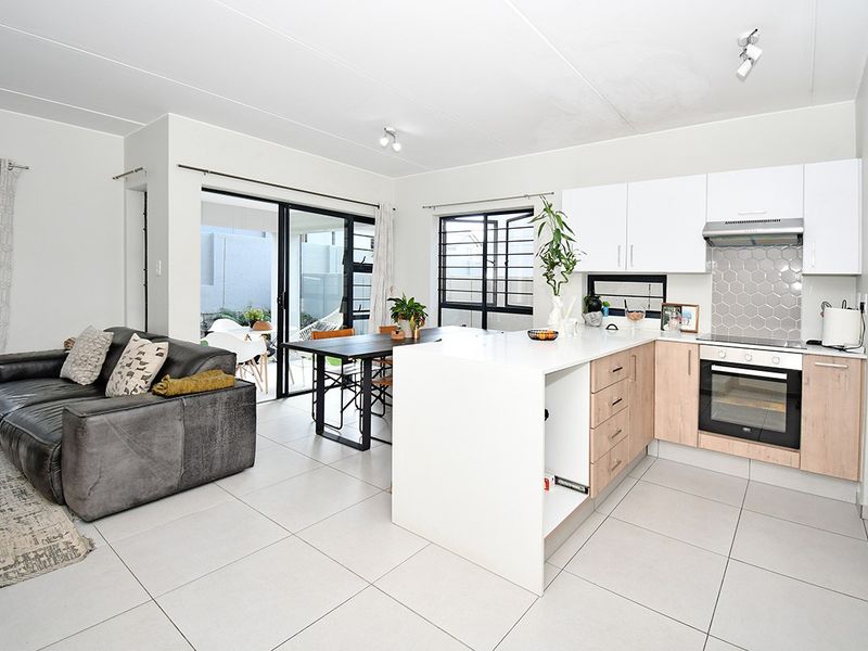 Modern open-plan living and kitchen area featuring a sleek kitchen island, built-in oven, hexagonal tile backsplash, and large sliding doors leading to the patio.