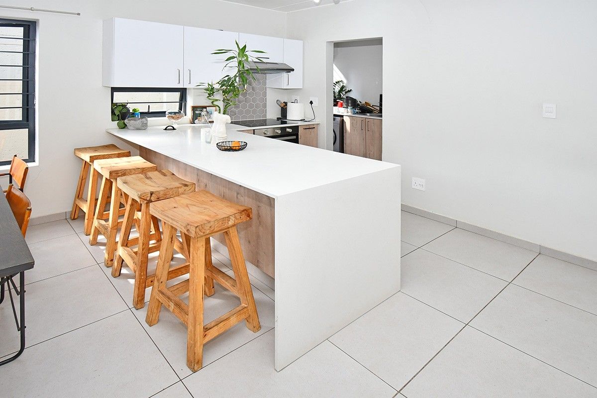 Modern kitchen featuring a large central island with stone countertop, built-in appliances, sleek white cabinetry, and neutral tiled flooring.