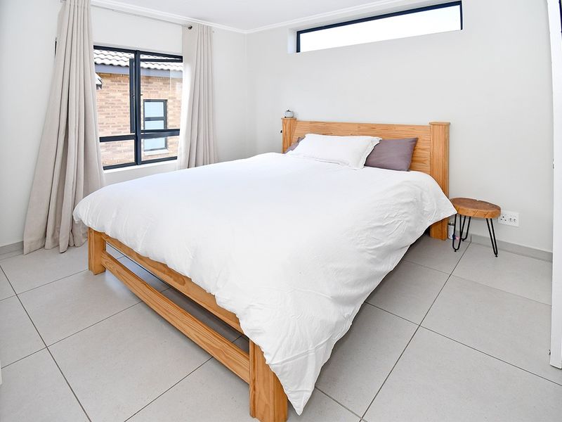 A bright and modern bedroom featuring neutral tiled flooring, a large casement window, and a high-level clerestory window for natural light.
