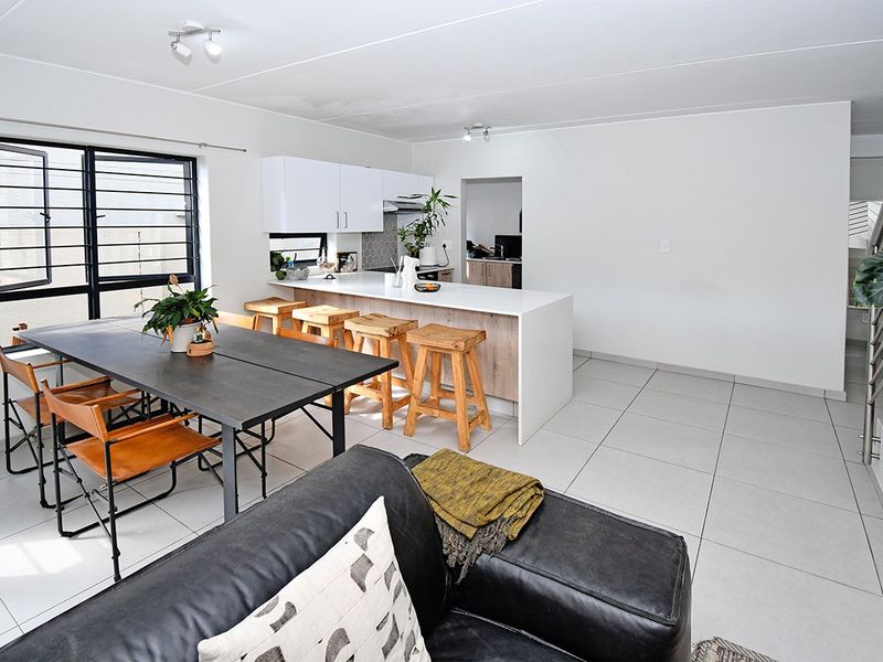 Open-plan living and dining area featuring a modern kitchen with a central island, tiled flooring, and a staircase leading to the upper level.