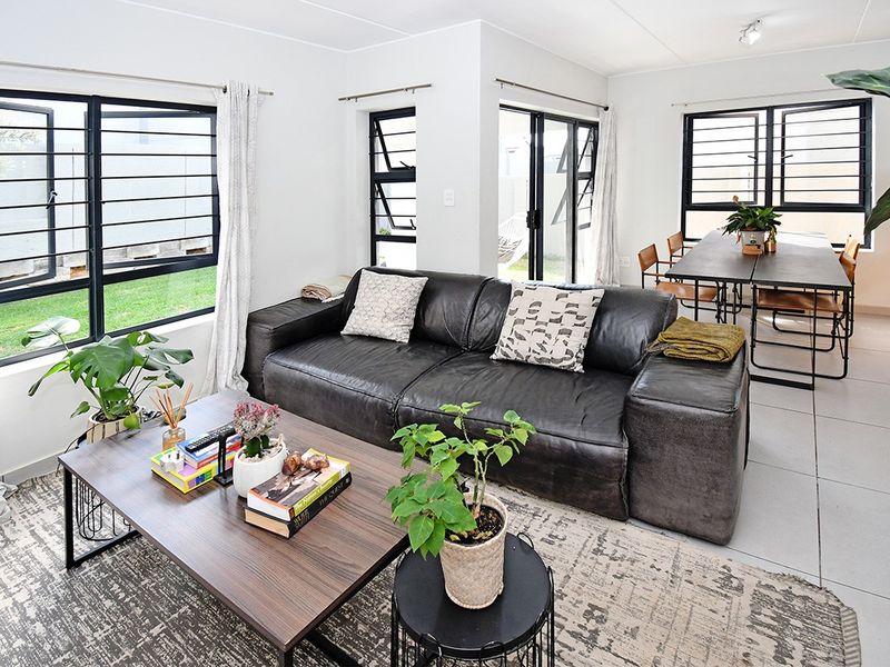Bright open-plan living and dining area featuring large windows with security bars, tiled flooring, and direct access to the outdoor space.