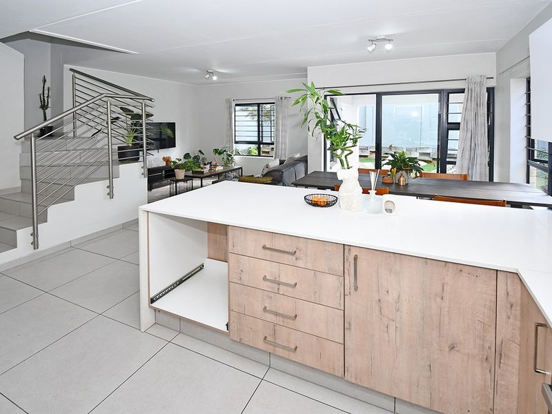 Open plan living area featuring a modern kitchen island, tiled flooring, and a staircase with a stainless steel balustrade leading to the upper level.