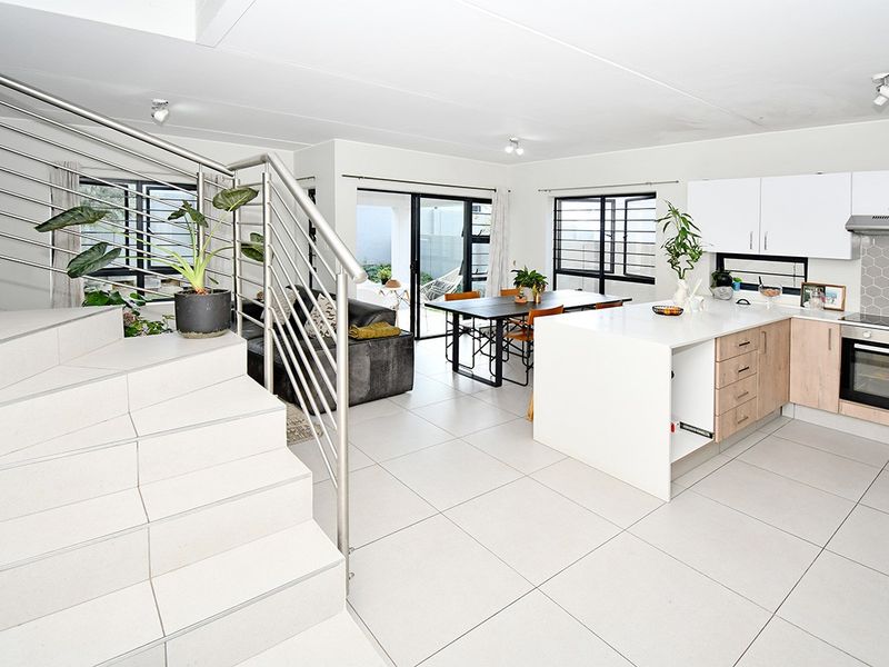 Spacious open-plan living and kitchen area featuring modern tiled floors, a central kitchen island, and direct access to the patio through sliding glass doors.