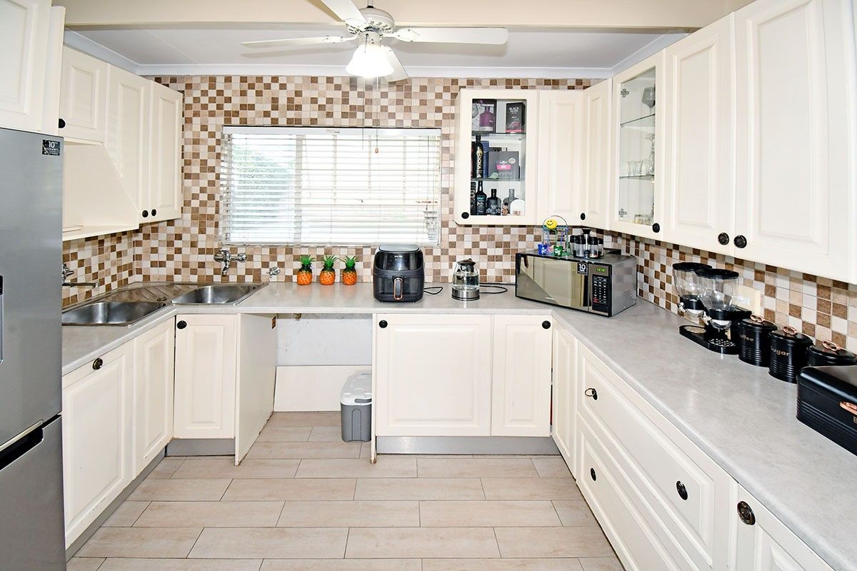 A functional kitchen featuring cream-colored cabinetry, tiled backsplash, laminate countertops, and a stainless steel double sink, with a ceiling fan for ventilation.