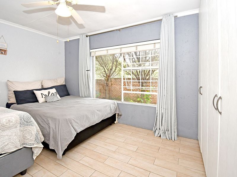 A well-lit bedroom featuring tiled flooring, built-in cupboards, and a ceiling fan, offering a comfortable and functional living space.