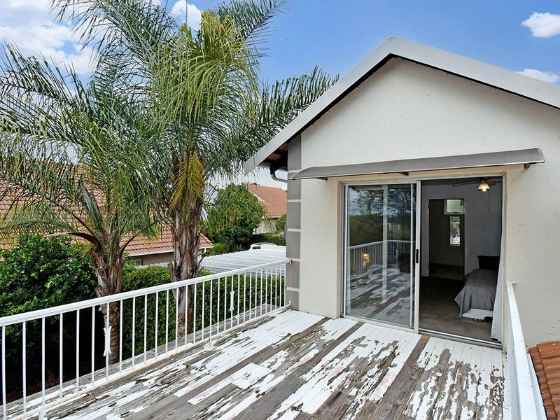 An elevated balcony featuring a sliding glass door, metal railing, and an awning, with the wooden decking showing significant signs of wear and peeling paint.