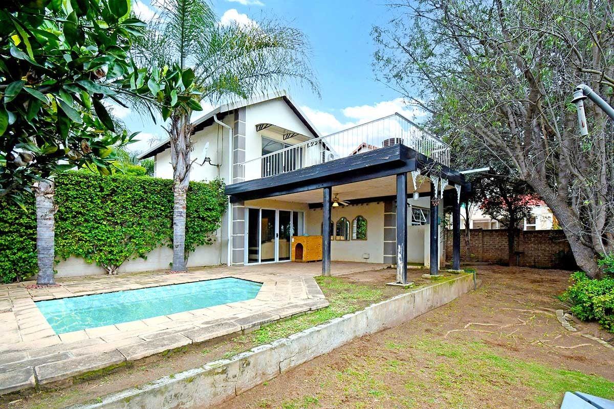 Rear view of the house featuring a swimming pool, a covered patio area, and an upper-level balcony with established garden surroundings.