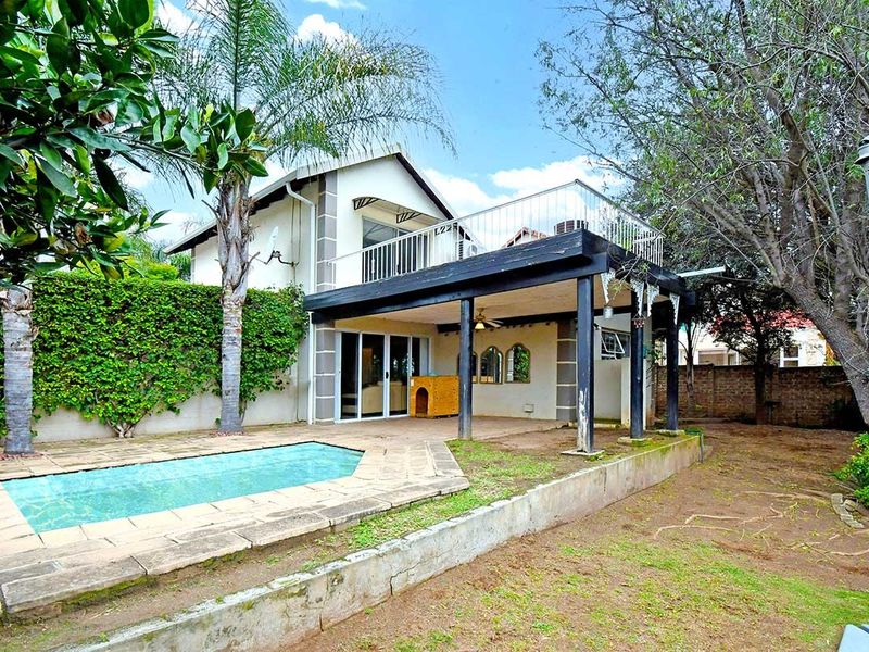 Rear view of the house featuring a swimming pool, a covered patio area, and an upper-level balcony with established garden surroundings.
