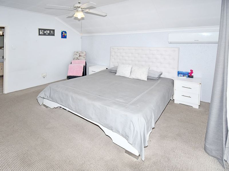 Spacious bedroom featuring neutral carpet flooring, a ceiling fan, and a wall-mounted split system air conditioner for climate control.