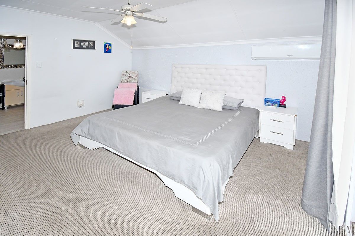 Spacious bedroom featuring neutral carpet flooring, a ceiling fan, and a wall-mounted split system air conditioner for climate control.