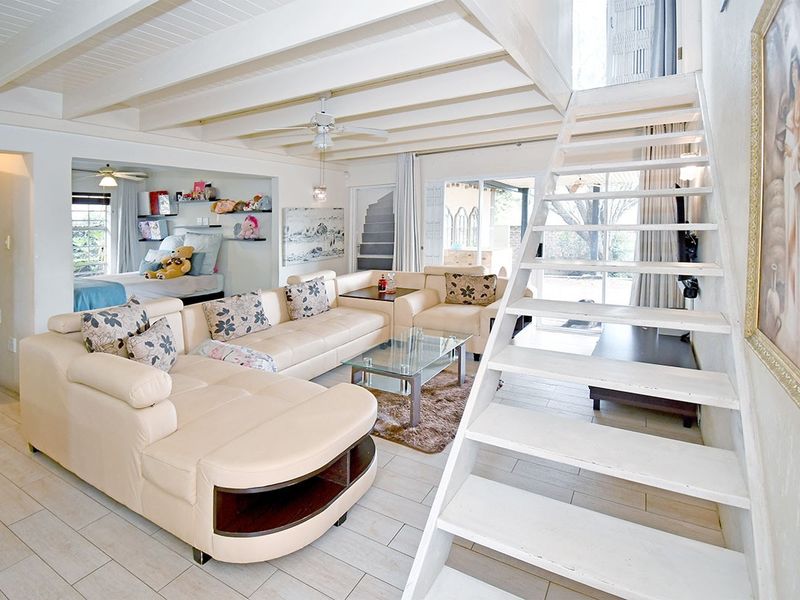 Open plan living area featuring exposed timber ceiling beams, tiled flooring, and a staircase leading to an upper level.