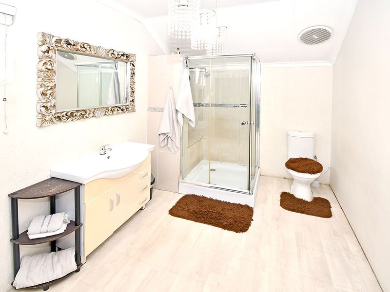 A functional bathroom featuring a vanity cabinet with basin, a glass-enclosed shower, and a standard toilet, finished with light-toned flooring.