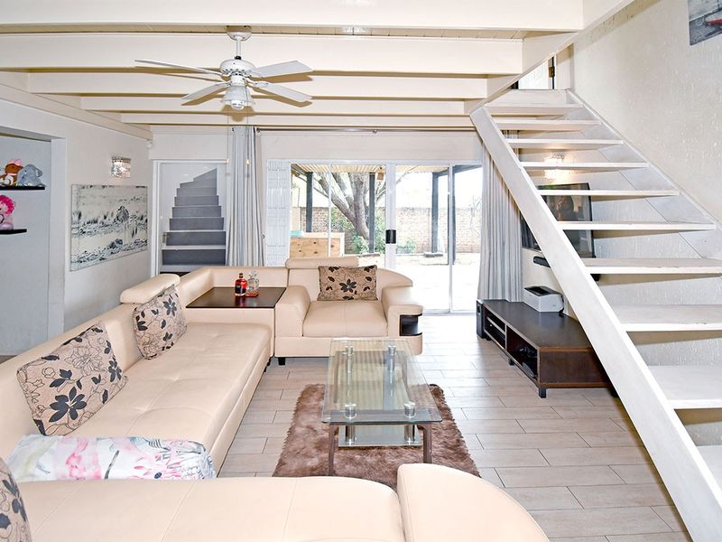 Spacious living room featuring exposed ceiling beams, a ceiling fan, tiled flooring, and a staircase leading to the upper level with access to the patio.