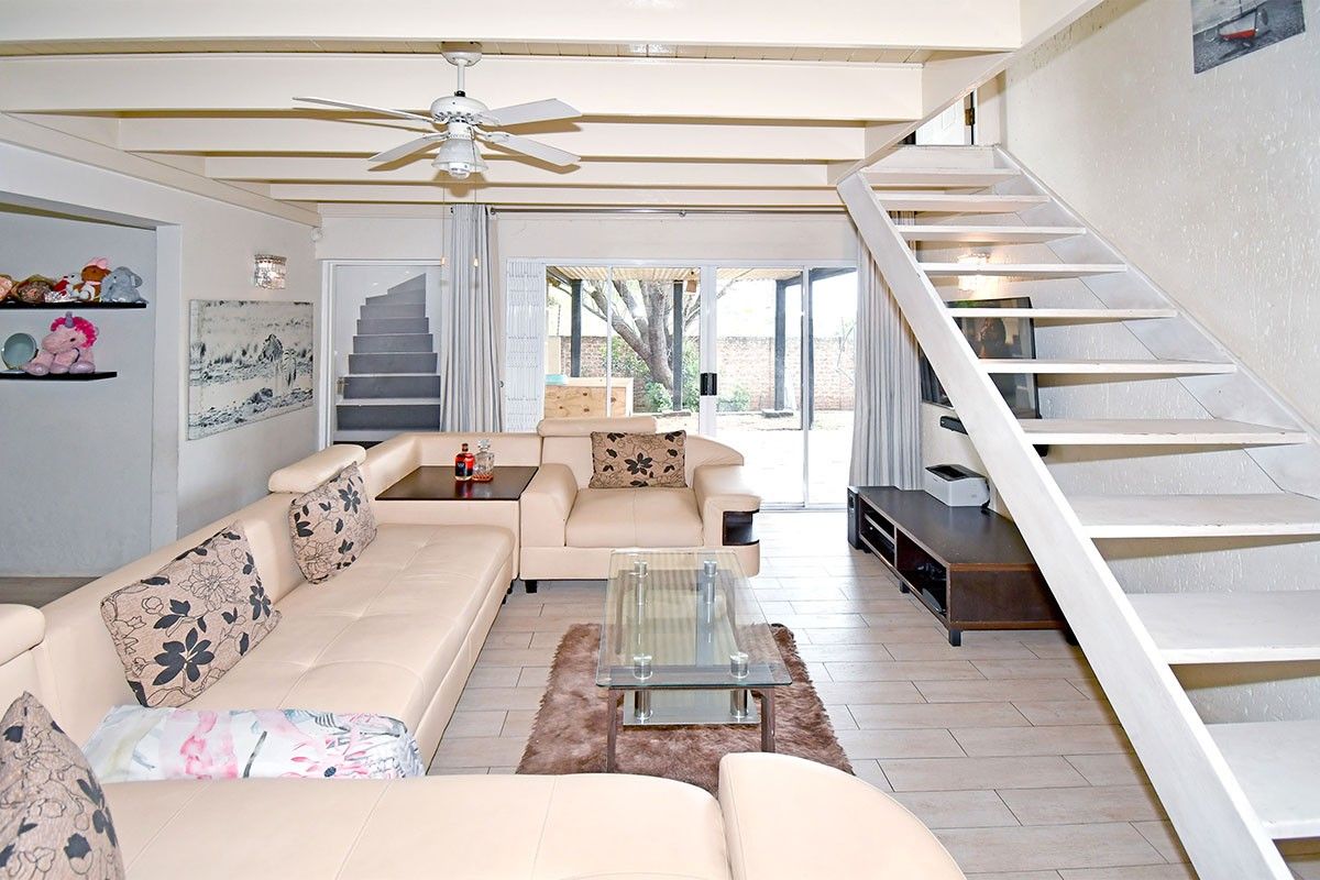 Spacious living room featuring exposed ceiling beams, a ceiling fan, tiled flooring, and a staircase leading to the upper level with access to the patio.