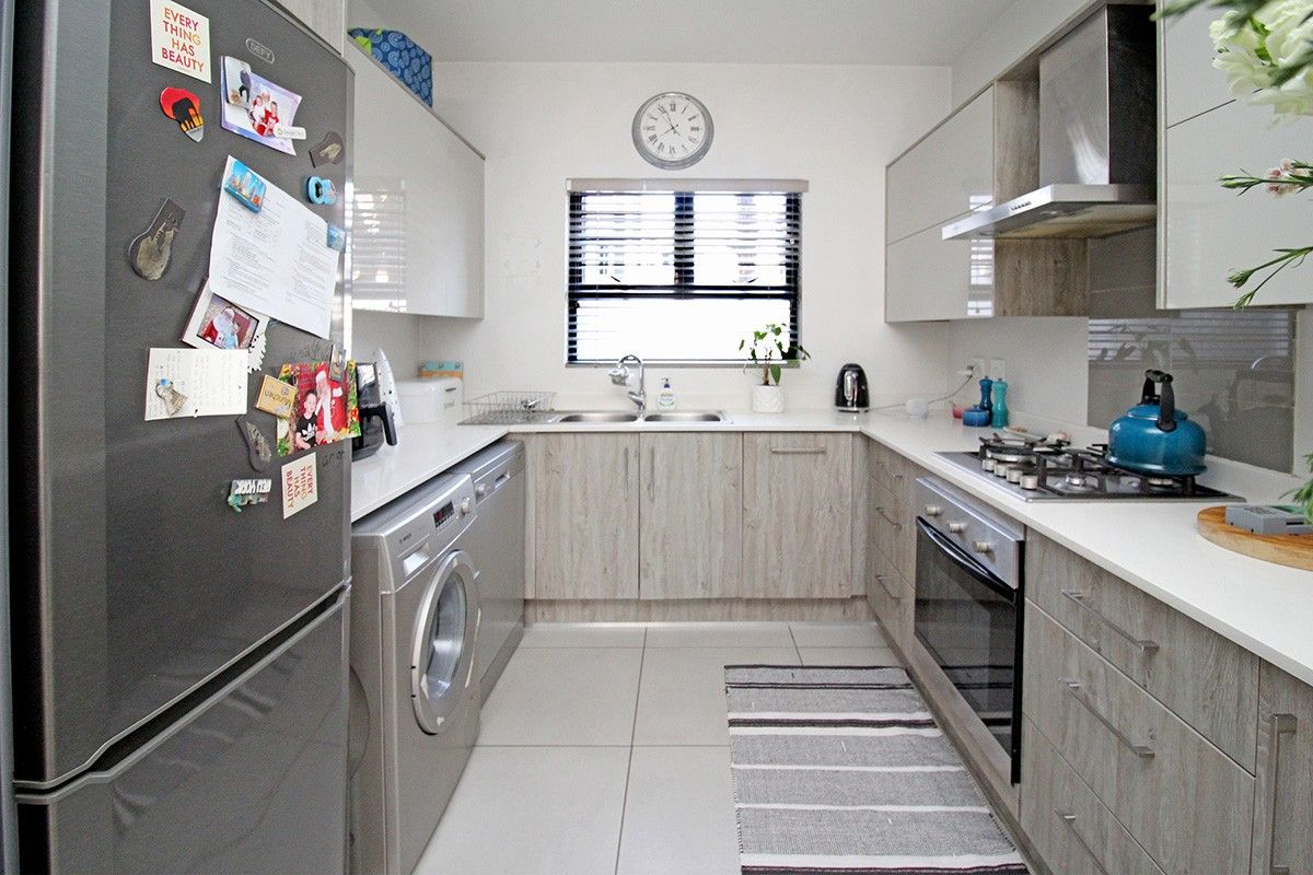 Modern galley-style kitchen featuring light wood-grain cabinetry, stone countertops, integrated gas hob, oven, and extractor fan with tiled flooring.