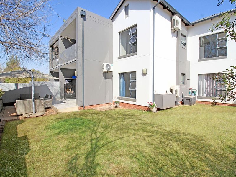Rear view of the apartment building featuring a private garden, paved patio area, and exterior air conditioning units.