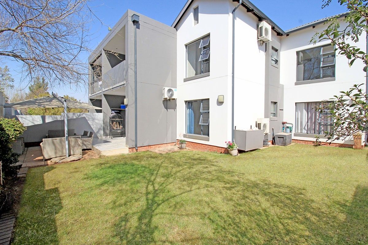 Rear view of the apartment building featuring a private garden, paved patio area, and exterior air conditioning units.