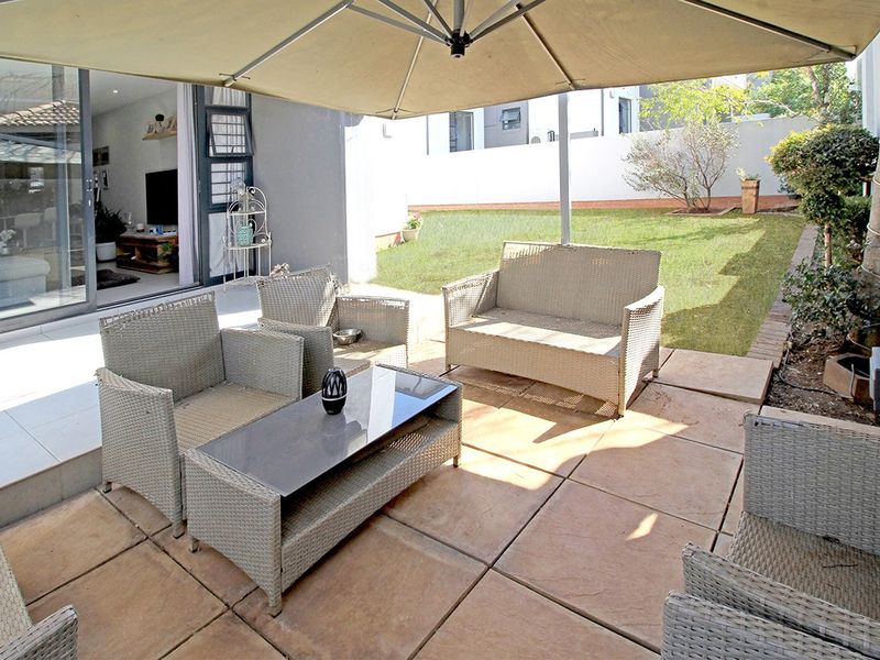 A paved outdoor patio area featuring sliding glass doors leading into the living space, overlooking a private garden lawn.
