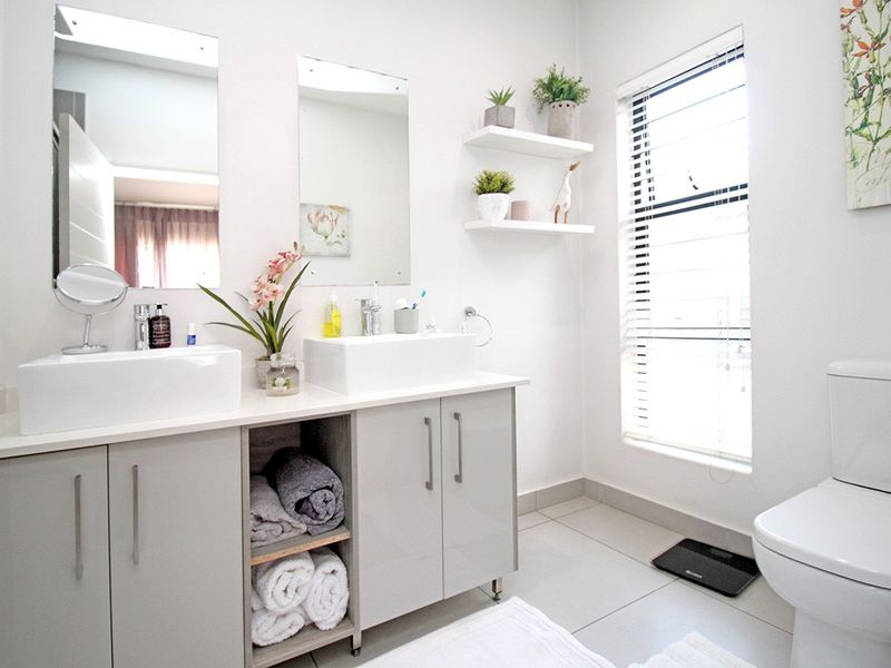Modern bathroom featuring a double vanity with vessel sinks, built-in cabinetry, floating shelves, and large ceramic floor tiles with natural light.
