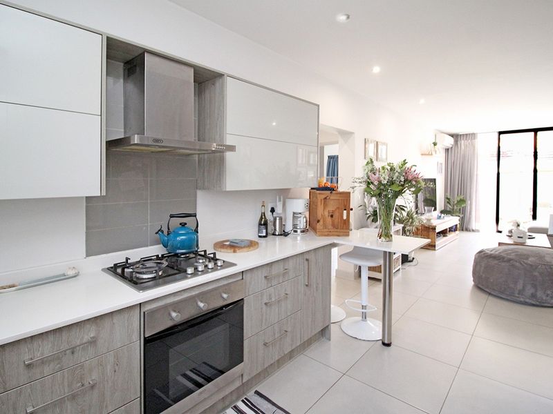 Modern open-plan kitchen featuring stone countertops, gas hob, built-in oven, and sleek cabinetry, flowing seamlessly into the living area with tiled flooring throughout.
