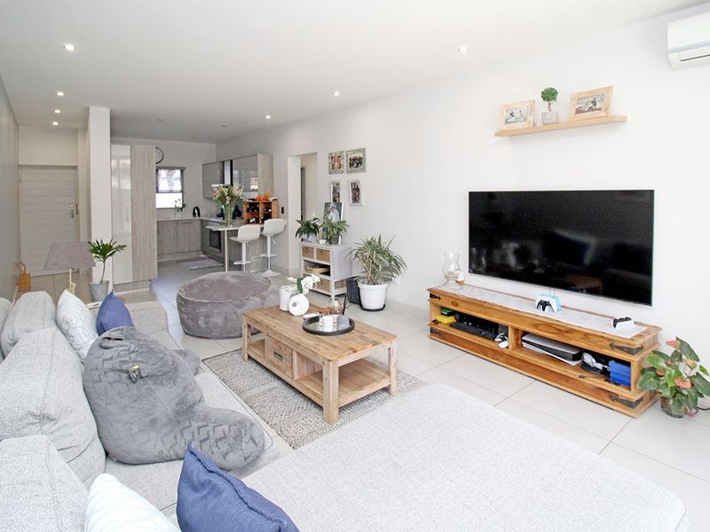 An open-plan living and kitchen area featuring neutral tiled flooring, recessed lighting, and a wall-mounted air conditioning unit.